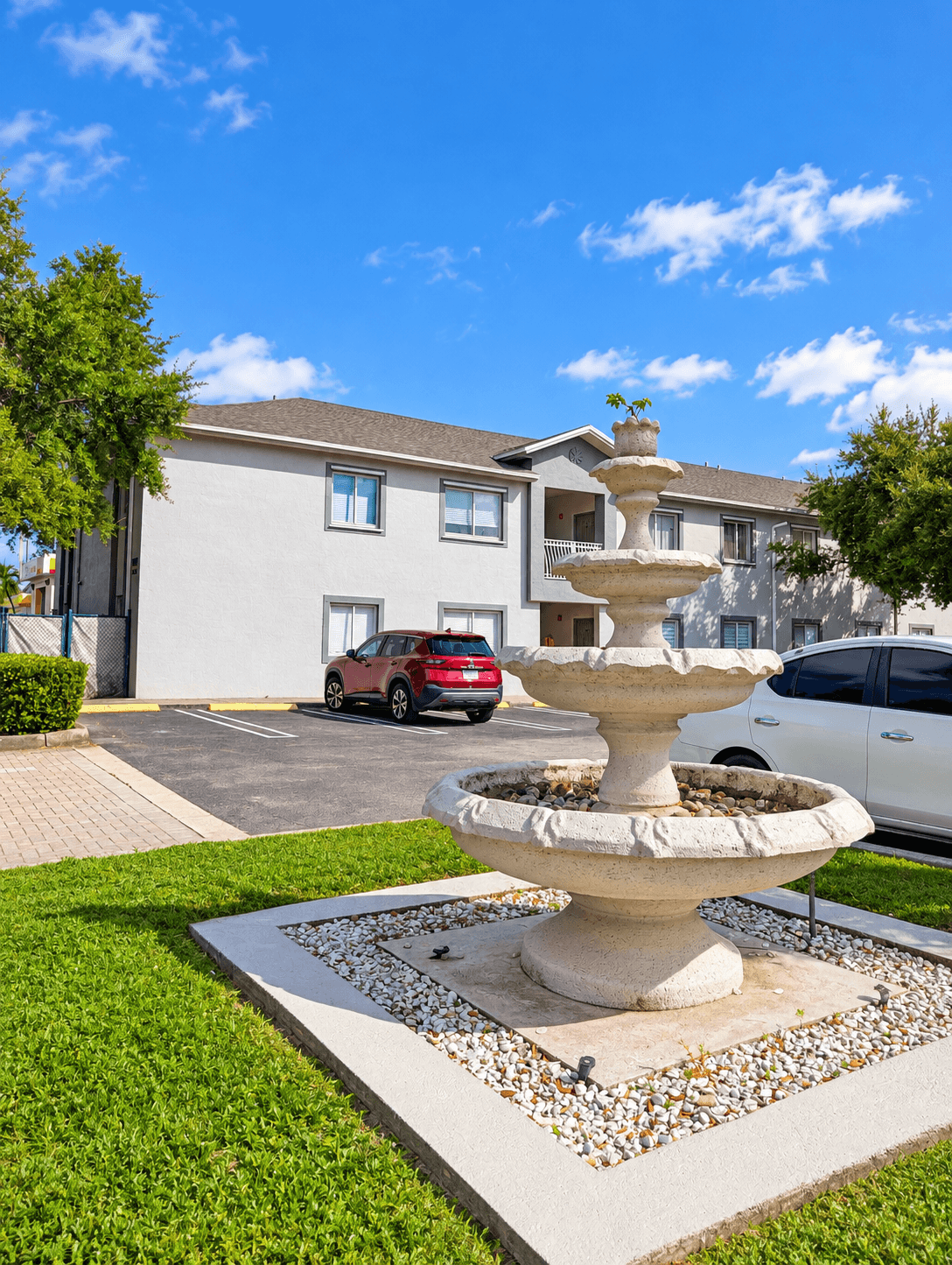 A white fountain in the middle of a grassy area in front of a building.